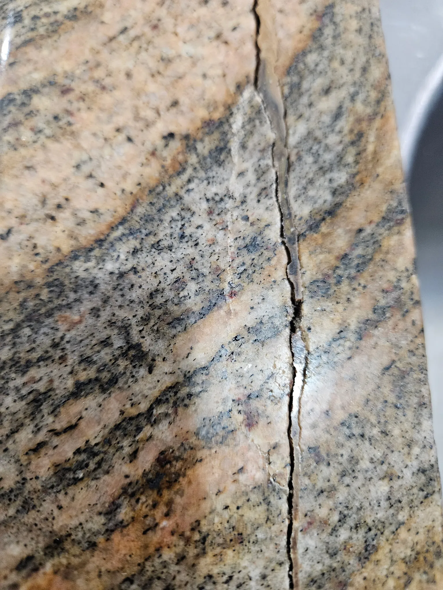 Close-up of deep crack in granite countertop showing stone separation and missing material
