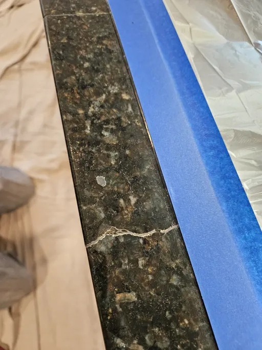 Dark granite edge crack before and after color-matched repair (before)