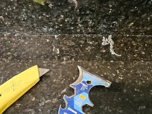 Old sealant being removed from dark granite