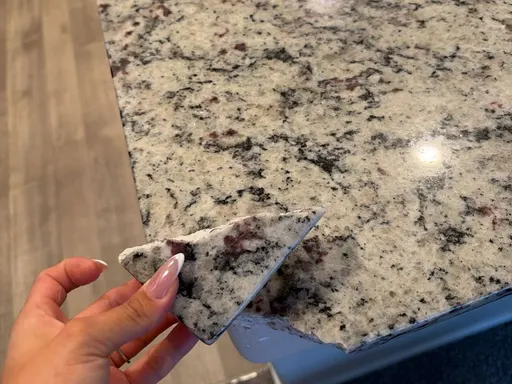 Corner chip broken off a granite countertop, with the broken piece held beside the edge
