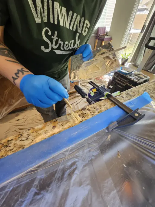 Technician filling and clamping a granite countertop crack with color-matched resin