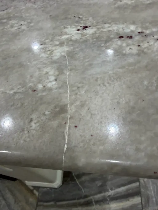Thin hairline crack running across a light granite countertop to the front edge