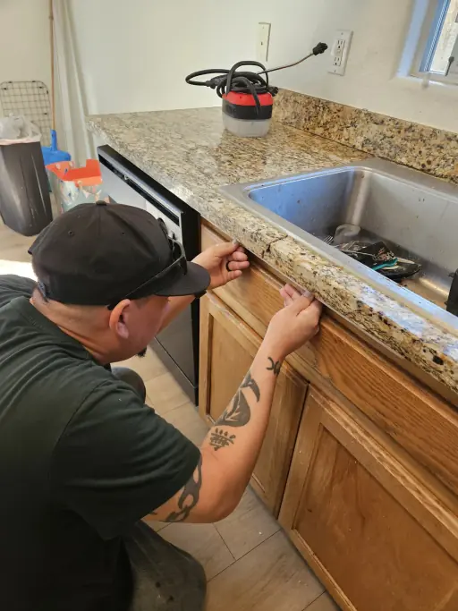 Technician inspecting a granite countertop edge beside the sink before restoration