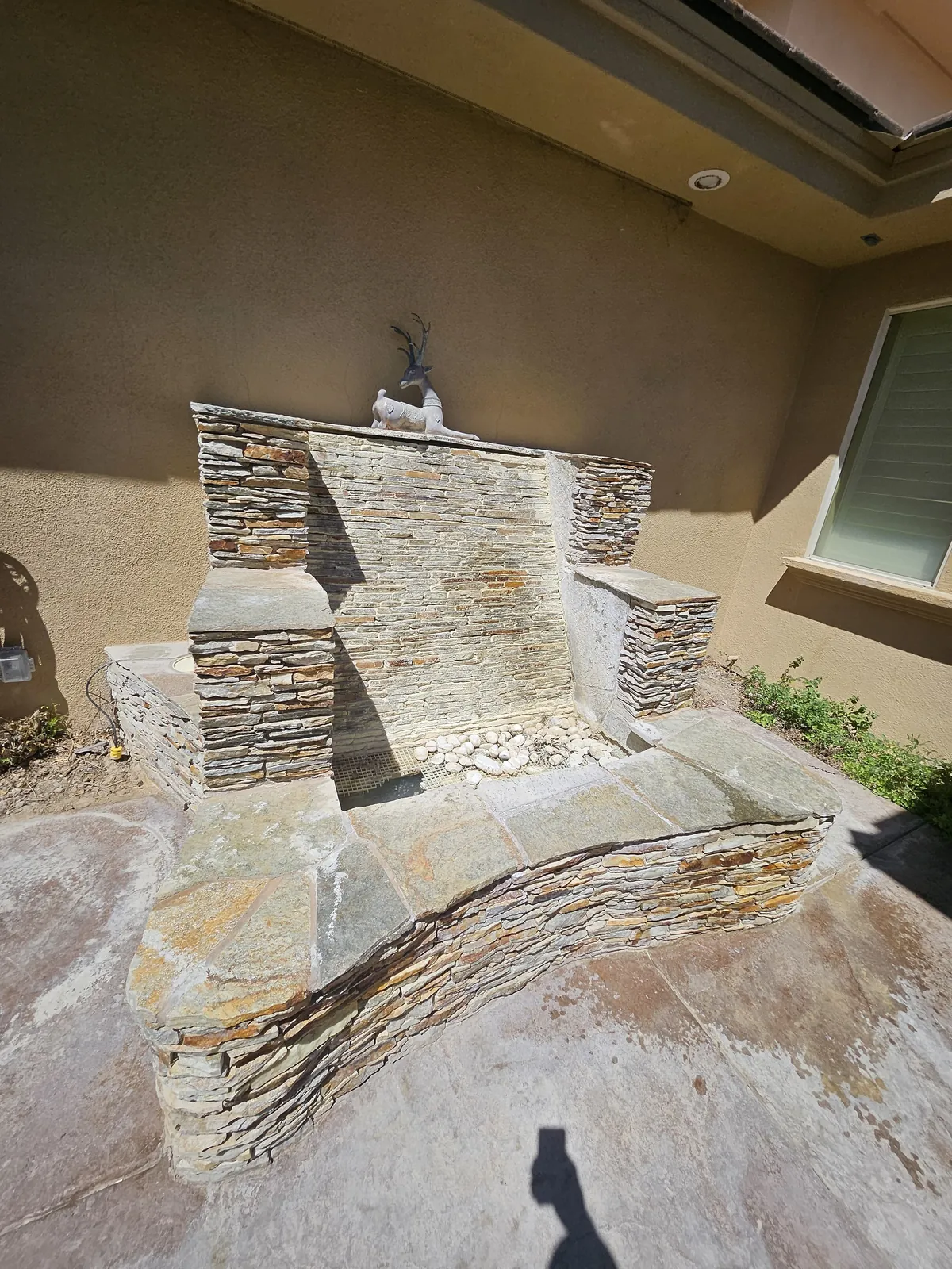 Front view of a restored stacked stone water feature with decorative deer statue