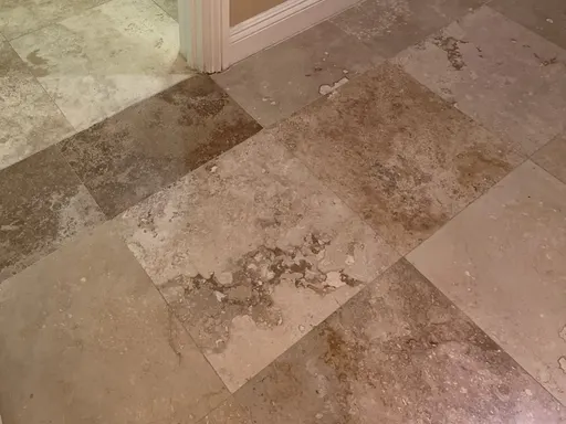 Customer photo of stained, worn travertine floor tiles near a doorway, sent for a quote