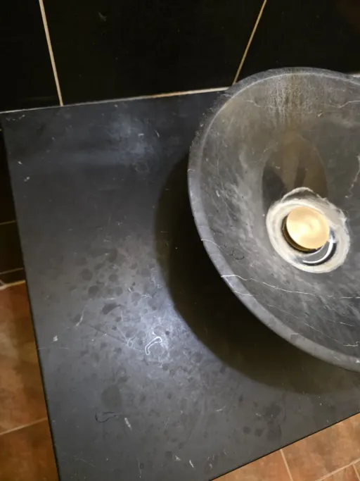 Hard water spots and mineral deposits on dark stone vanity